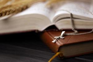 colar de prata com cruz crucifixo no livro da bíblia sagrada cristão na mesa de madeira preta. pedindo bênçãos de Deus com o poder da santidade foto