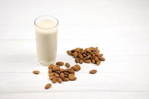 copo de leite de amêndoa com amêndoas na mesa de madeira branca. leite alternativo de laticínios para desintoxicação, alimentação saudável e dietas foto