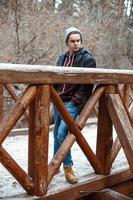 jovem bonito fica em uma ponte de madeira no fundo da floresta de inverno foto
