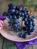 galho de uvas azuis em um copo em um prato