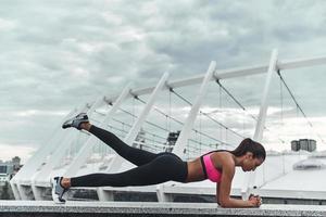 treino matinal. mulher jovem e moderna em roupas esportivas, mantendo a posição de prancha durante o exercício ao ar livre foto