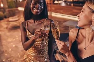 duas mulheres bonitas em vestidos de noite brindando com champanhe e sorrindo foto