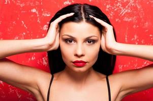 fogo em seus olhos. retrato de mulher jovem e bonita olhando para a câmera e segurando o cabelo de íon de mão em pé contra um fundo vermelho foto