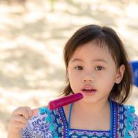 retrato de uma linda menina asiática de 4 anos de idade, criança pequena com lindos olhos brilhantes come sorvete Olhe para a câmera com espaço de cópia. foto