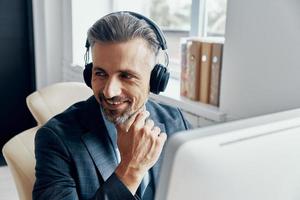 empresário bonito em fones de ouvido sorrindo enquanto está sentado em seu local de trabalho foto