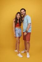 comprimento total do lindo casal jovem sorrindo em pé contra um fundo amarelo foto
