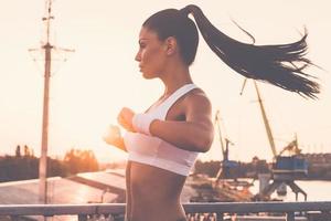 aquecimento antes de correr. mulher jovem e bonita em roupas esportivas fazendo exercícios de alongamento e olhando concentrado em pé na ponte foto