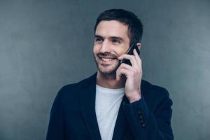 boa conversa de negócios. jovem alegre falando no celular e sorrindo em pé contra um fundo cinza foto