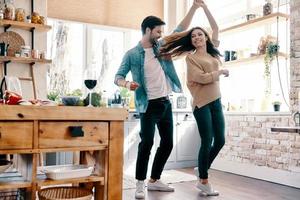 dois corações cheios de amor. comprimento total do lindo casal jovem em roupas casuais dançando e sorrindo em pé na cozinha em casa foto