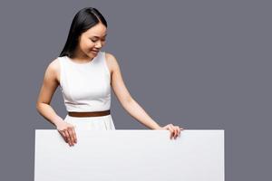 beleza curiosa. bela jovem mulher asiática olhando para o espaço da cópia e sorrindo em pé contra um fundo cinza foto