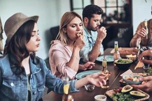 deixar todas as preocupações para trás. grupo de jovens em roupas casuais comendo enquanto faz um jantar dentro de casa foto