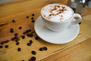 cappuccino quente em copo branco com fundo de madeira, o café é uma bebida popular em todo o mundo. foto