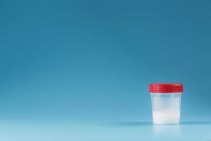 sêmen em um recipiente de teste com tampa vermelha sobre fundo azul. foto