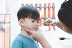 mãe asiática corta o cabelo do filho sozinha em casa. idéias de corte de cabelo feliz para crianças. as mães ficam felizes em cortar o cabelo de seus filhos. foto