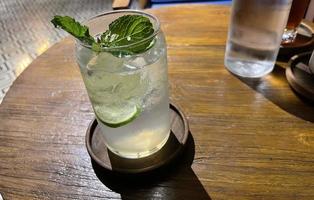 foco seletivo, delicioso mojito de verão refrescante com gelo, limão e hortelã em um copo com grops. fundo de madeira foto