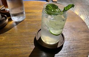 foco seletivo, delicioso mojito de verão refrescante com gelo, limão e hortelã em um copo com grops. fundo de madeira foto