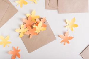 folhas de maple amarelo e laranja de papel em um envelope de artesanato em um fundo rosa. vista do topo. foto