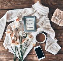 conceito de blogueiro. tiro de alto ângulo de suéter, flores, xícara de café, caixa de presente, telefone inteligente e moldura na mesa de madeira foto