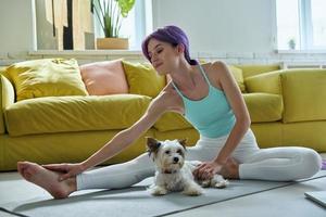 jovem confiante em roupas esportivas fazendo exercícios de alongamento com seu cachorro em casa foto