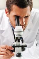 vida ao microscópio. concentrado jovem cientista em uniforme branco usando microscópio enquanto trabalhava no laboratório foto