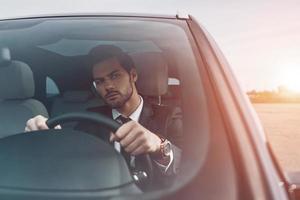 Motorista cuidadoso. jovem bonito de terno completo olhando em linha reta enquanto dirigia um carro foto