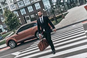 jovem empresário. comprimento total de jovem de terno completo atravessando a rua enquanto caminhava ao ar livre foto