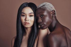 beleza multiétnica. mulheres jovens atraentes olhando para a câmera em pé contra um fundo marrom foto