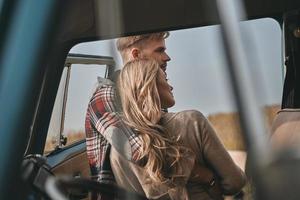 sempre protegendo ela... lindo casal jovem abraçando ao ar livre perto da mini van estilo retrô foto