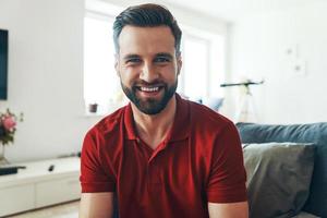 jovem bonito em roupas casuais, olhando para a câmera e sorrindo enquanto passa o tempo dentro de casa foto