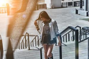 beleza em movimento. mulher jovem e bonita em roupas casuais, tocando seu cabelo enquanto subia as escadas ao ar livre foto