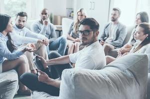 treinador de vida confiante. grupo de jovens sentados em círculo e discutindo algo enquanto jovem segurando tablet digital e olhando por cima do ombro foto