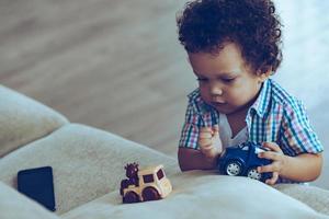 meninos adoram trenzinhos. bebezinho africano brincando com brinquedos em pé perto do sofá em casa foto