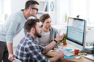 colaboração é a chave para o sucesso. três jovens empresários discutindo algo enquanto olham para o monitor do computador juntos foto