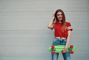 menina feliz. bela jovem olhando para a câmera e carregando skate em pé ao ar livre foto