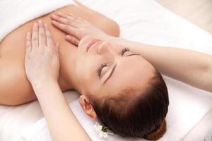 desfrutando de massagem no spa. vista superior da bela jovem deitada de costas e mantendo os olhos fechados enquanto massagista massageando-a foto