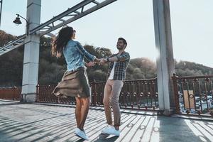 sentimentos puros. comprimento total do lindo casal jovem de mãos dadas e girando em pé na ponte ao ar livre foto