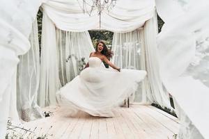 impossível esconder sua felicidade. comprimento total de mulher jovem e atraente em vestido de noiva gritando enquanto dançava no pavilhão de casamento ao ar livre foto