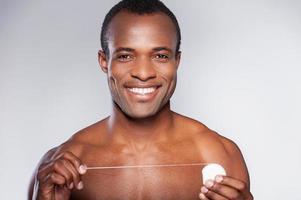 bonito com fio dental. retrato de jovem africano sem camisa segurando fio dental e sorrindo em pé contra um fundo cinza foto