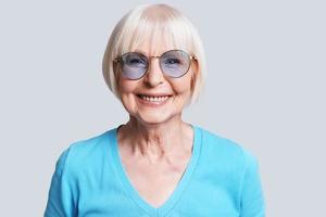 fêmea sênior na moda. linda mulher sênior olhando para a câmera e sorrindo em pé contra um fundo cinza foto