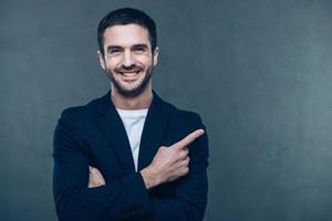 sua publicidade aqui. jovem alegre apontando para o espaço de cópia e sorrindo em pé contra um fundo cinza foto