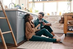 o amor está no ar. lindo casal jovem bebendo vinho enquanto está sentado no chão da cozinha em casa foto
