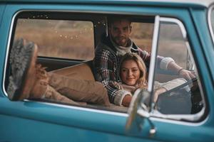 melhor viagem de todos os tempos. mulher jovem e atraente descansando e sorrindo enquanto o namorado dirigindo mini van estilo retrô foto