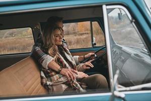 casal aventureiro. lindo casal jovem abraçando e sorrindo enquanto está sentado na mini van azul estilo retrô foto
