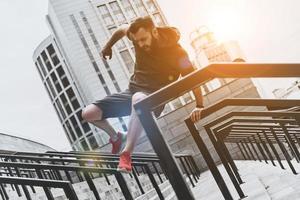 o esporte é o caminho de sua vida. vista de ângulo baixo de jovem bonito em roupas esportivas pulando sobre trilhos durante o exercício fora foto