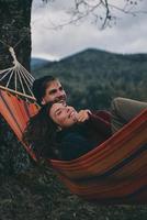 totalmente feliz. lindo casal jovem abraçando e sorrindo enquanto estava deitado na rede debaixo da árvore foto