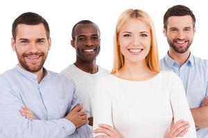 feliz por ser uma equipe. quatro jovens felizes em roupas casuais inteligentes, olhando para a câmera enquanto se unem e estão em pé contra um fundo branco foto