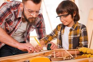 trabalhadores talentosos. concentrado jovem carpinteiro masculino ensinando seu filho a trabalhar com madeira em sua oficina foto