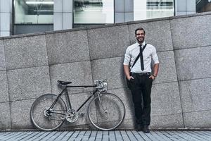 empresário moderno. jovem bonito de terno completo, olhando para a câmera e sorrindo em pé ao ar livre foto