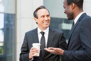 pausa para o café. dois homens de negócios alegres conversando ao ar livre enquanto um deles segurando uma xícara de café foto