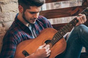 acorde perfeito. close-up de jovem bonito tocando violão enquanto está sentado no parapeito da janela foto